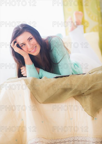 Portrait of woman lying down on bed with head in hands