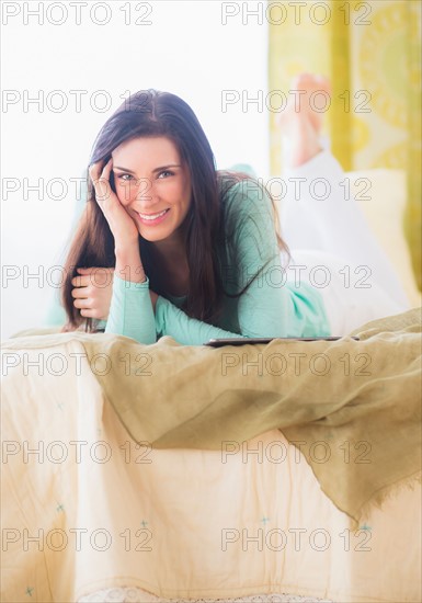 Portrait of woman lying down on bed with head in hands