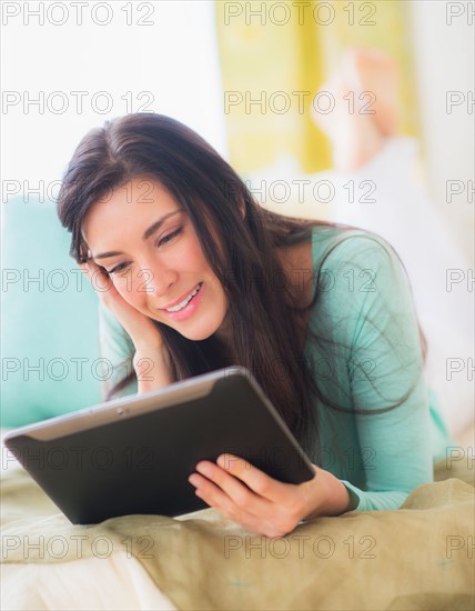 Portrait of woman lying down on bed using tablet pc, Close-up