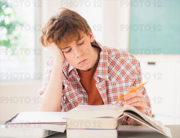 Teenage boy (14-15) sitting in classroom with pencil and books