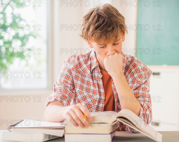 Teenage boy (14-15) sitting in classroom with pencil and books