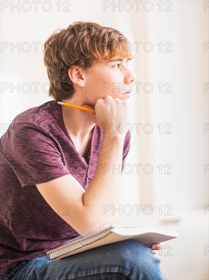 Teenage boy (14-15) sitting and holding pencil and note pad