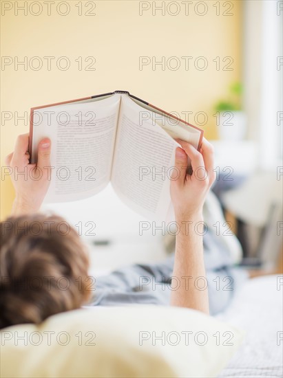 Teenage boy (14-15) lying on bed and reading book