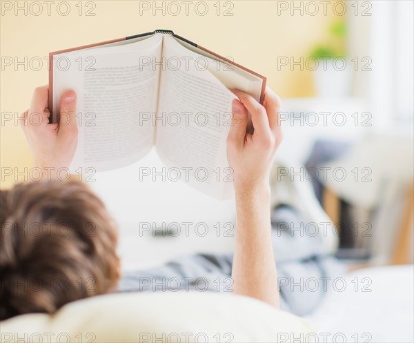 Teenage boy (14-15) lying on bed and reading book