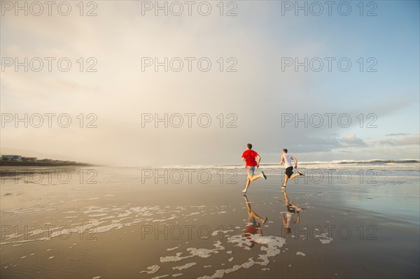 Young adult men running on beach