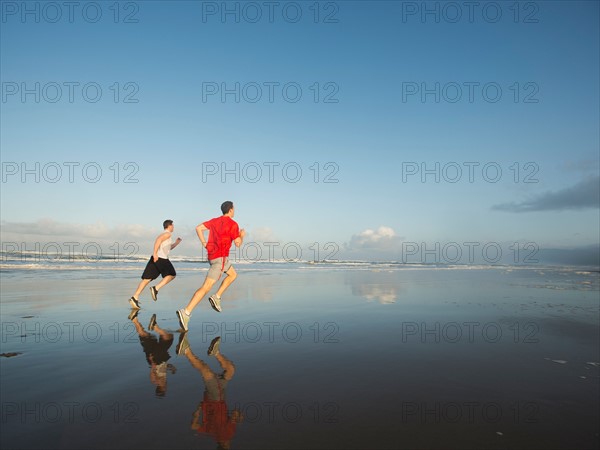 Young adult men running on beach