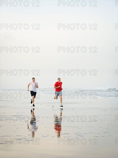 Young adult men running on beach