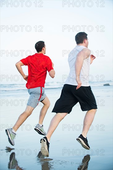 Young adult men running on beach