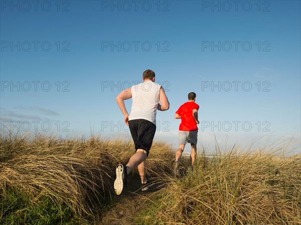 Young adult men running on dune