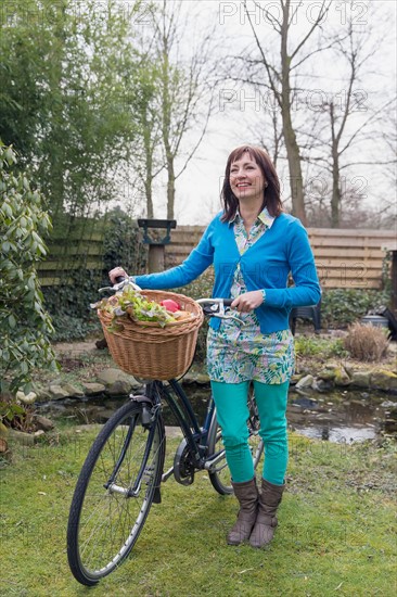 Mature woman with fresh vegetables in bike basket