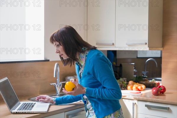 Mature woman using laptop while cooking