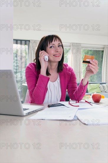 Mature businesswoman talking on phone and using credit card