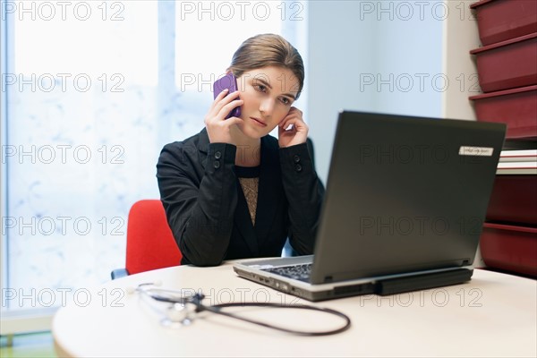 Woman working on laptop and talking on cell phone