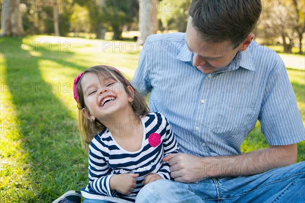 Father tickling his daughter (4-5 years) on sunny day in park