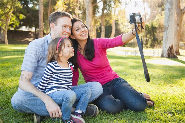 Family with daughter (4-5) playing in park and photographing themselves