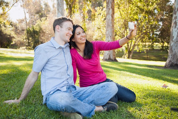 Couple sitting on grass in park photographing themselves