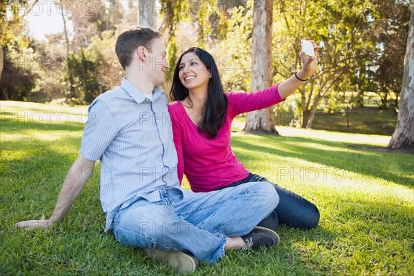 Couple sitting on grass in park photographing themselves