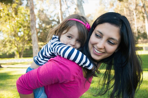 Portrait of mother giving her daughter (4-5) piggy back ride in park