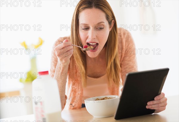 Woman eating breakfast and looking at tablet pc.