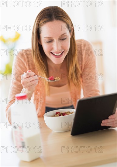 Woman eating breakfast and looking at tablet pc.