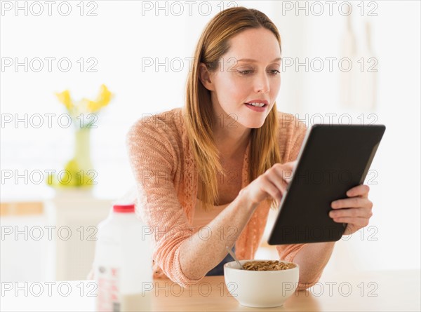 Woman eating breakfast and looking at tablet pc.