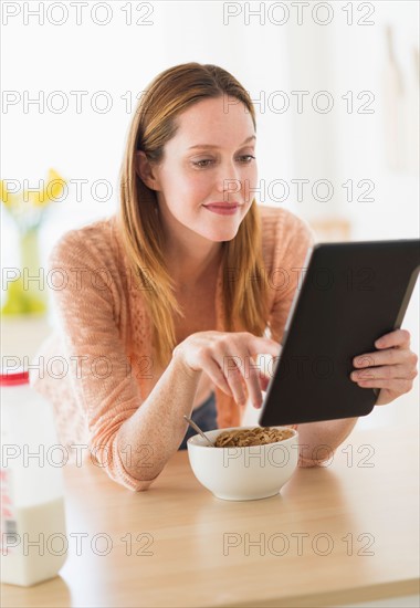 Woman eating breakfast and looking at tablet pc.