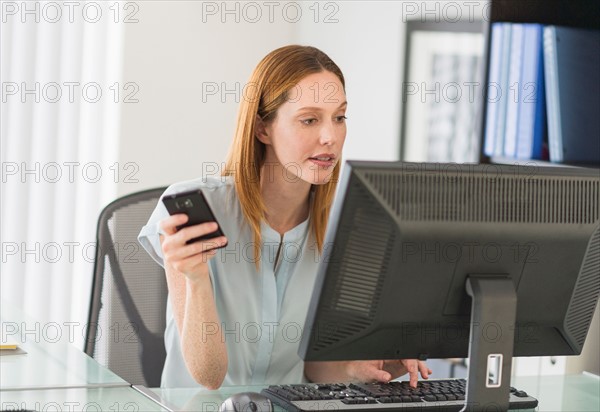 Business woman using computer and phone in office.