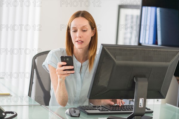 Business woman using computer and phone in office.