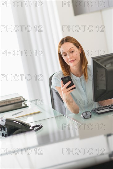 Business woman using computer and phone in office.