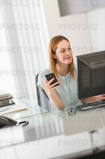 Business woman using computer and phone in office.