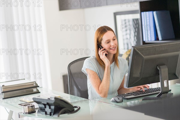 Business woman using computer and phone in office.