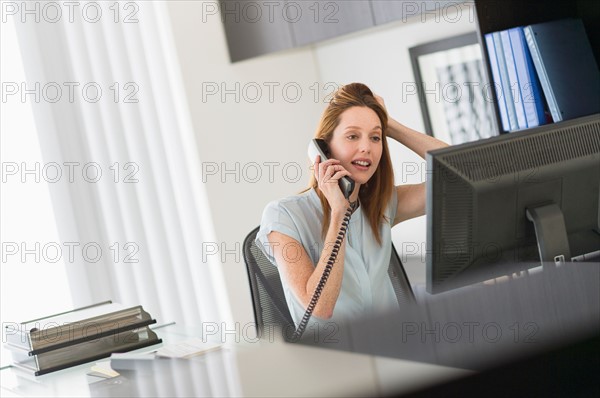 Business woman using computer and phone in office.