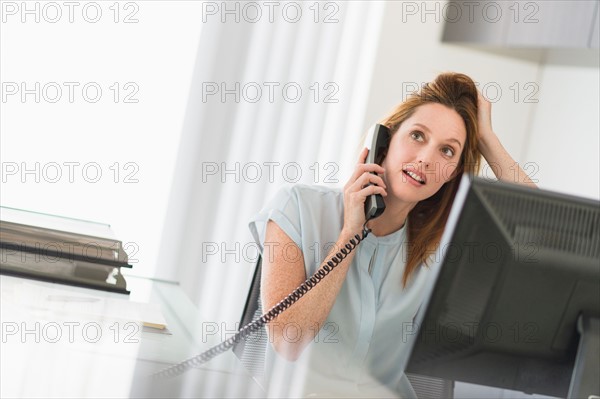 Business woman using computer and phone in office.