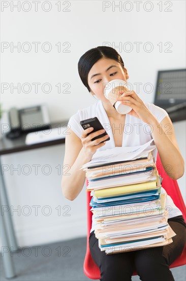 Businesswoman with stack of files texting on phone.