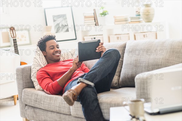 Man lying on sofa and using tablet PC.