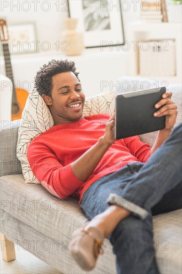 Man lying on sofa and using tablet PC.