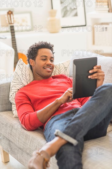 Man lying on sofa and using tablet PC.