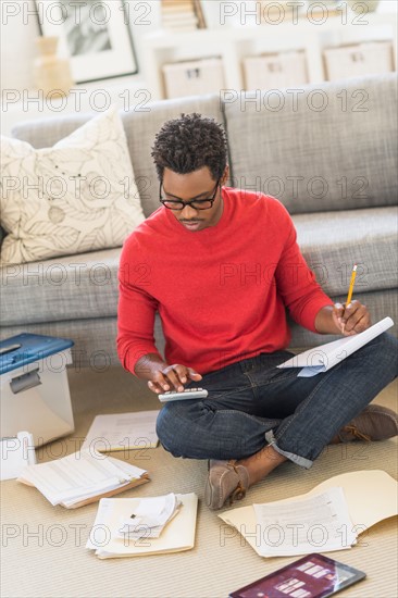 Man sitting on floor in living room and calculating bills.