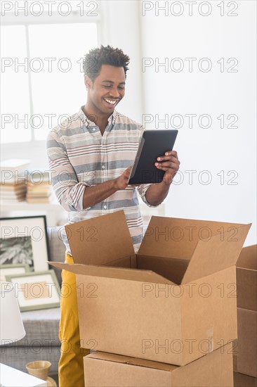 Man using tablet PC while unpacking cardboard box.