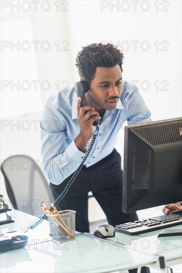 Businessman working on computer and talking on cell phone.