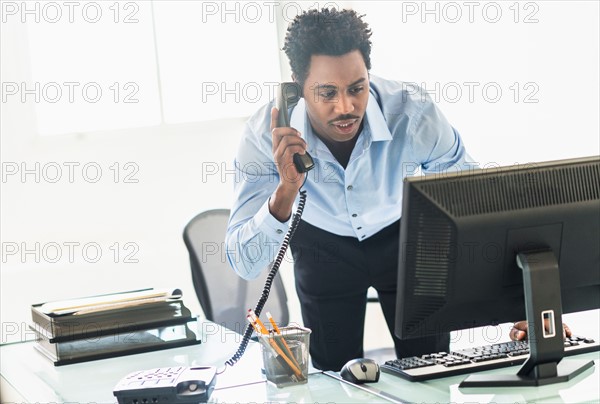 Businessman working on computer and talking on cell phone.