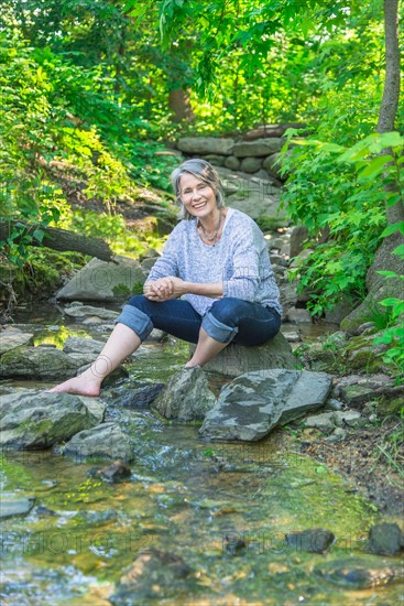 Central Park, New York City. Senior woman sitting by stream.