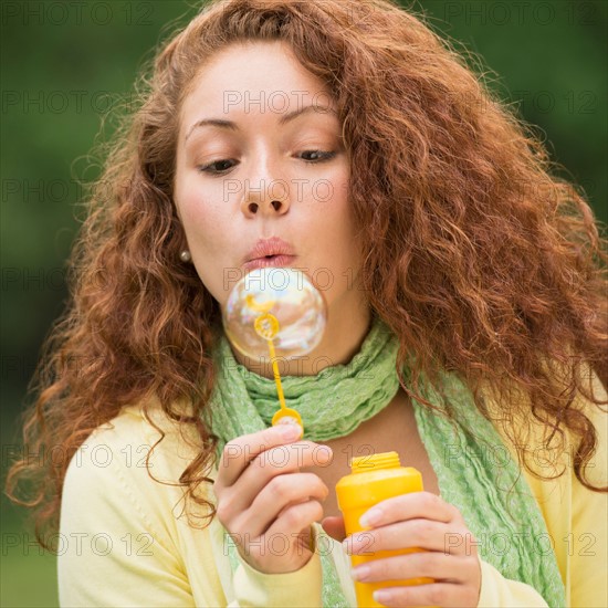 Young woman blowing bubbles in park.