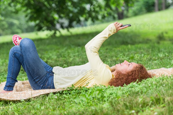 Woman lying on grass in park and using mobile phone.