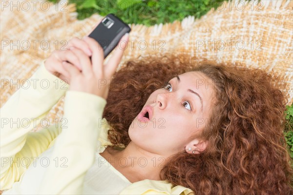 Woman lying on grass in park and using mobile phone.