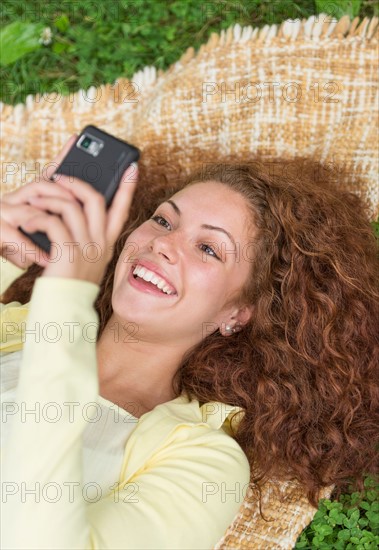 Woman lying on grass in park and using mobile phone.