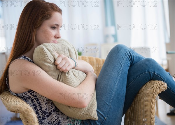 Teenage girl (14-15) sitting sad in armchair