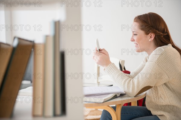 Teenage girl (14-15) using mobile phone in library