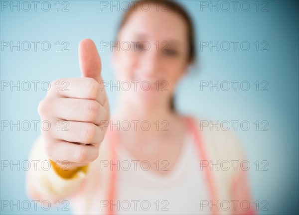 Teenage girl (14-15) showing thumb up, studio shot