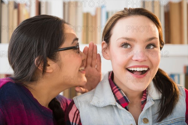 Young woman whispering to friends ear